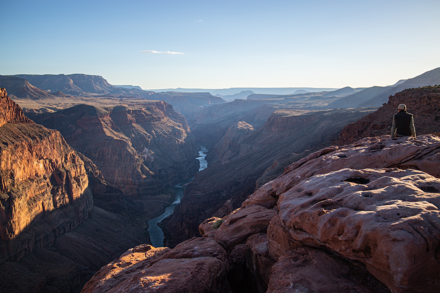 A hiker sits at the top of the Grand Canyon watching the sunset — nationaparks